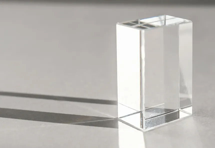 Clear glass rectangular prism casting a shadow on a smooth surface under bright lighting.